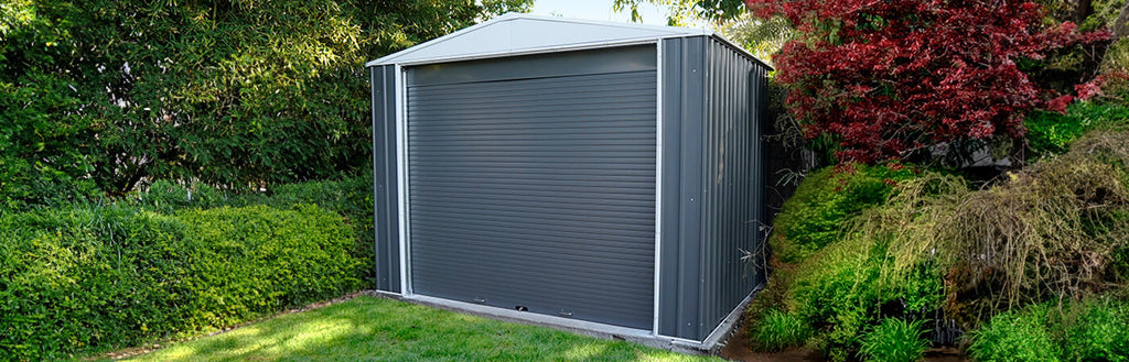 A large steel shed with a roller door in a backyard