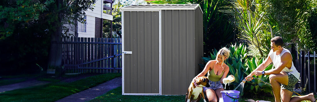 A couple washing a dog in front of a steel garden shed in a backyard